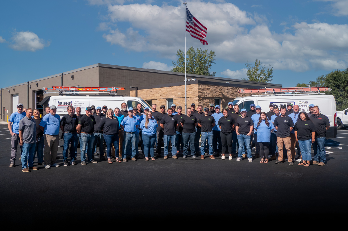 Davis Mechanical team standing in front of service trucks with an American flag flying in the background