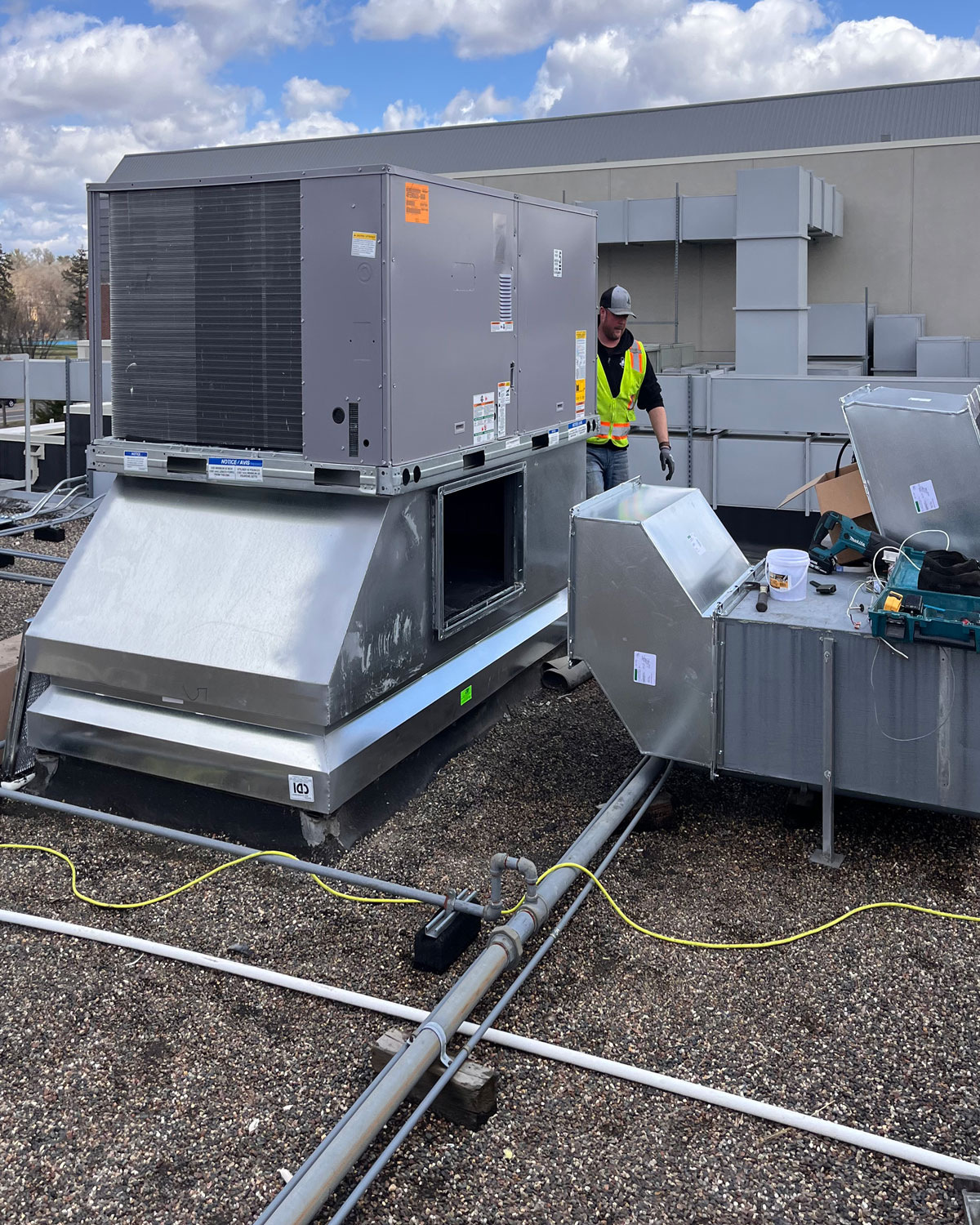 Man wearing a neon yellow vest performing equipment maintenance for HVAC on a commercial rooftop